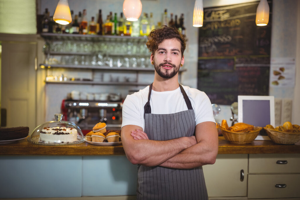 Smiling waiter standing with arms crossed in Cafe